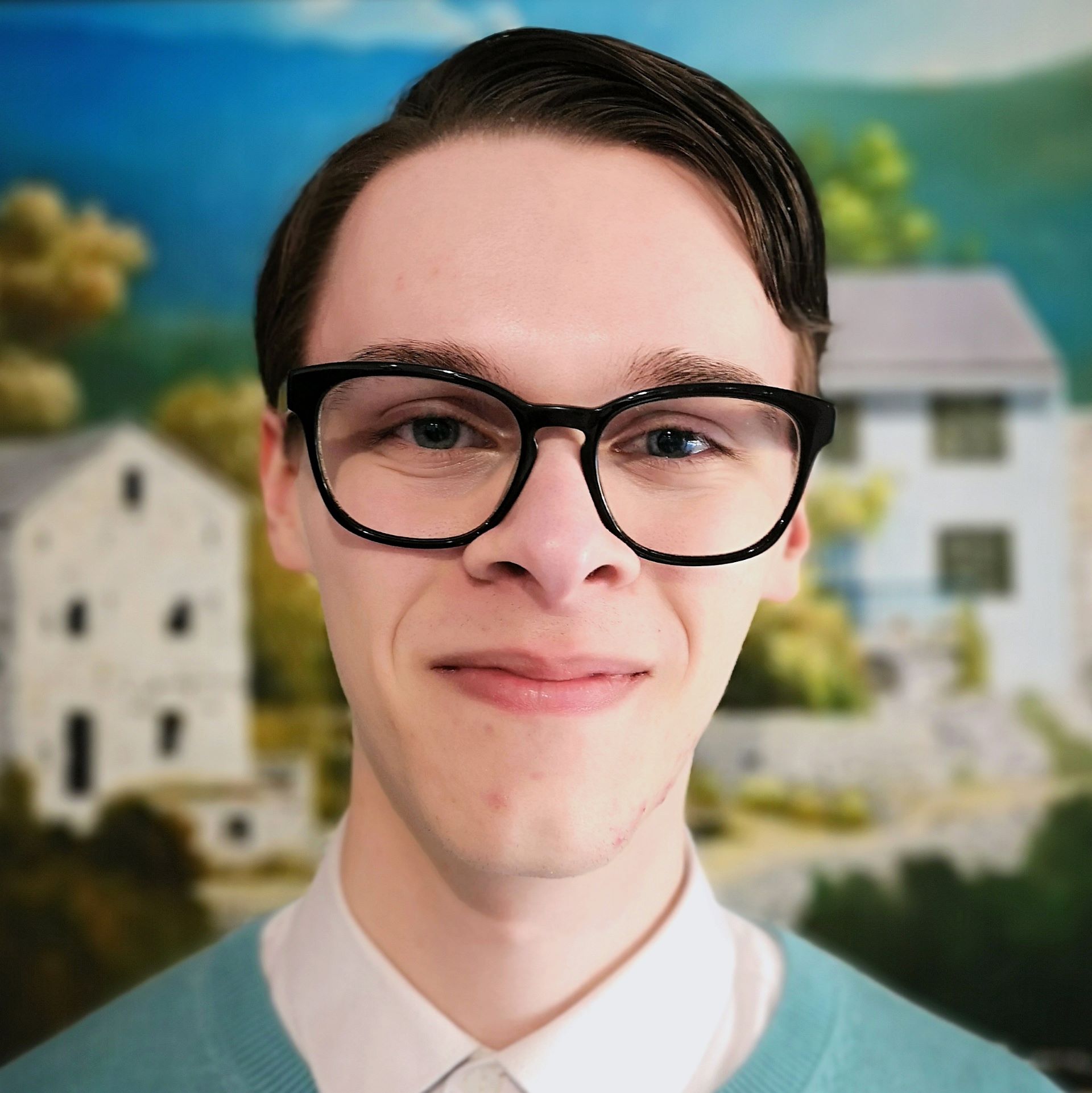 Image of Julian with brown hair, black glasses,
																				a white shirt, and blue jumper standing in front
																				of a scenery painting